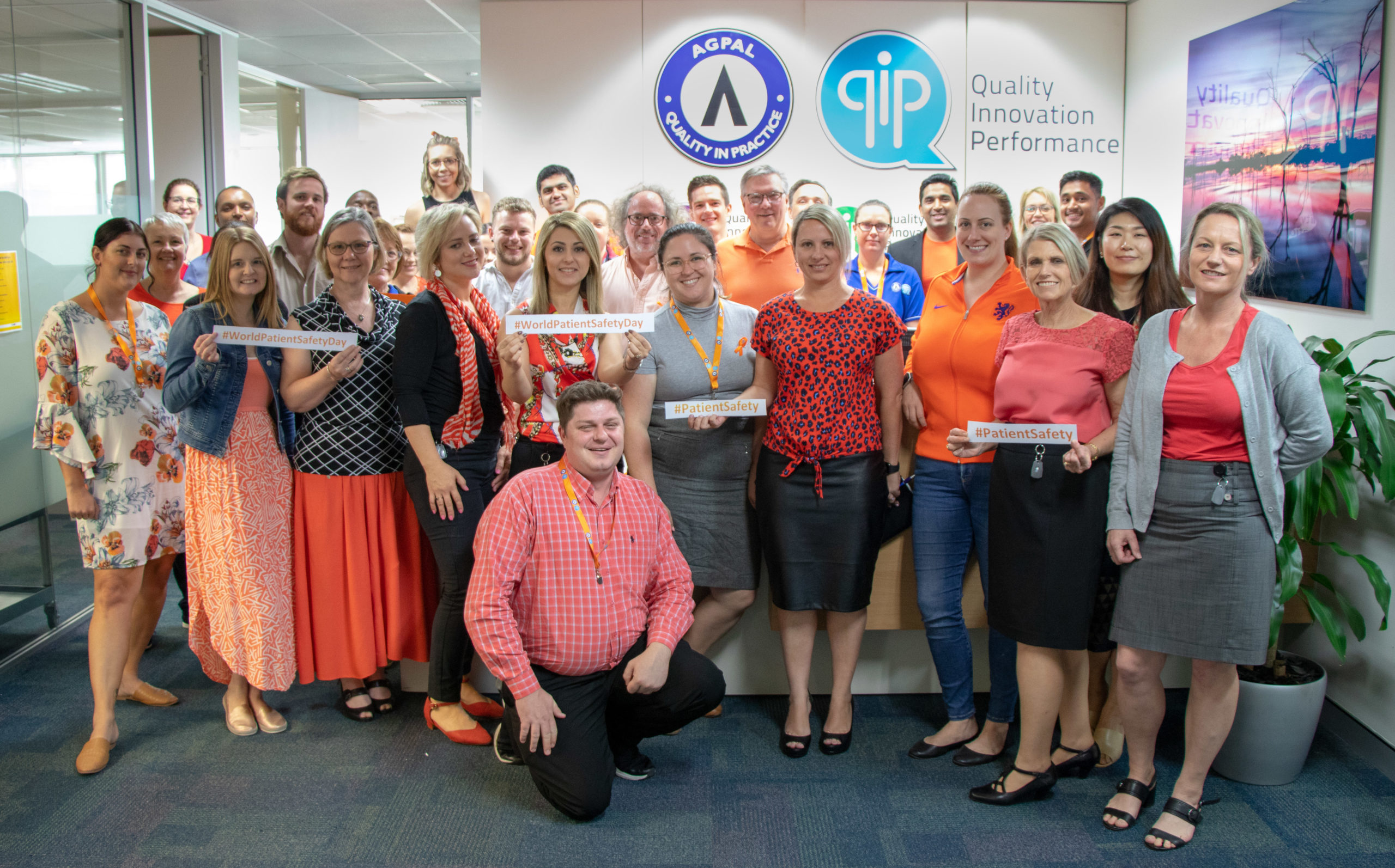 Group photo of smiling AGPAL staff dressed in orange with company logo in the background
