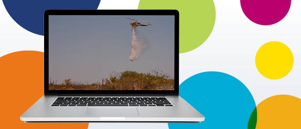 Header image with colourful circle background, with a computer featuring a picture of a bushfire-fighting helicopter dropping water over land