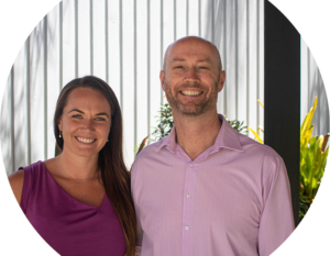 Image of a business woman and man both wearing shades of purple smiling near a garden