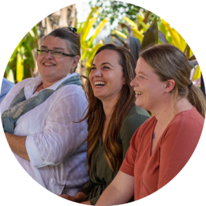 Image of three women sitting on a bench near a garden smiling