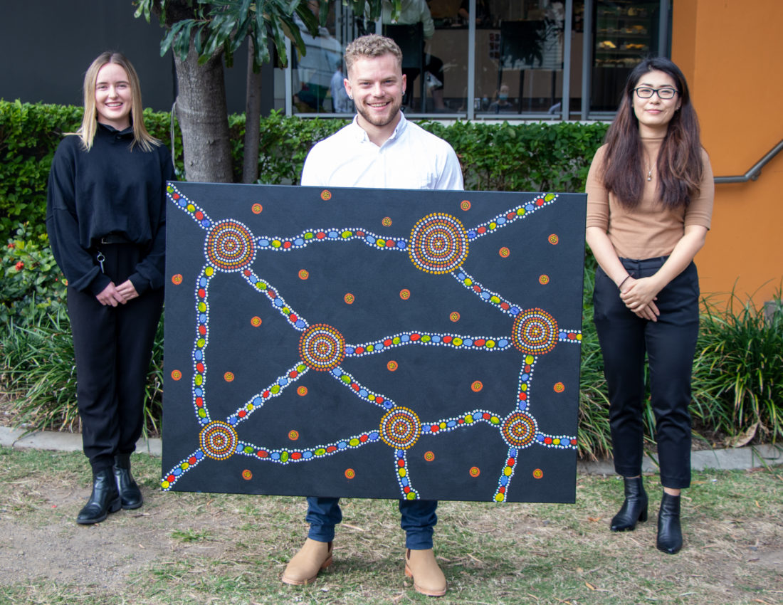 Three AGPAL and QIP staff holding a piece of Indigenous art painting by the staff for NAIDOC Week 2021