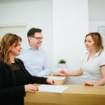At clinic Positive young couple talking with secretary at reception in the clinic