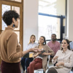 Pretty stylish woman lecturer giving presentation to a group of businesspeople.