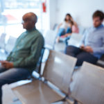 Defocused image of people at waiting room. Patients are waiting at hospital. They are sitting on seat.