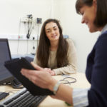 Consultant Discussing Test Results With Patient Consultant Discussing Test Results With Patient In Doctor's Surgery Smiling