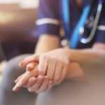 A female nurse consoles a senior patient at home