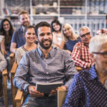 Large group of happy entrepreneurs attending a business conference in board room. Focus is on young man with beard.