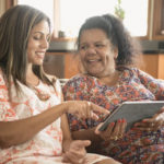 Two women using digital tablet smiling and laughing Aboriginal young woman showing her mother how to use tablet, pointing at the screen
